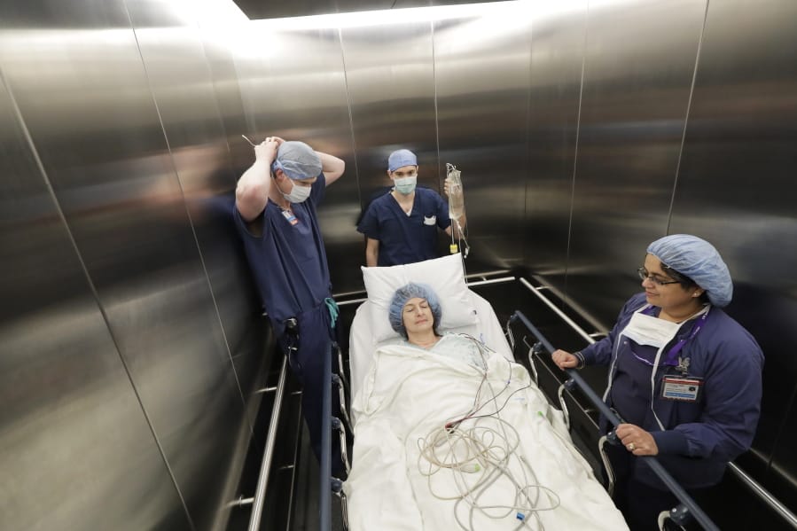 In this Jan. 14, 2020 photo, Genette Hofmann, center, is transported in an elevator by medical staff at Harborview Medical Center in Seattle just before undergoing brain surgery in hopes of reducing the epileptic seizures that had disrupted her life for decades. At the same time, Hofmann agreed to donate a small bit of her healthy brain tissue to researchers. The decision to contribute to the study was simple, even beyond her own epilepsy. She spent years caring for a grandmother with dementia. &quot;It was the easiest decision I&#039;ve ever made,&quot; she said. &quot;This will be my chance to make a difference.&quot; (AP Photo/Ted S.