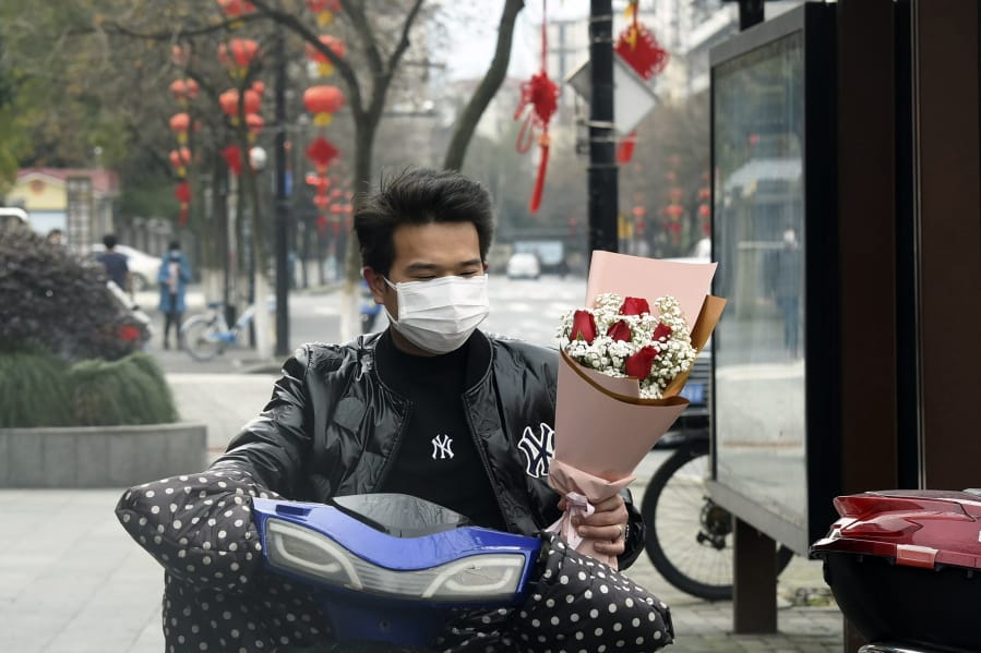 A man wearing a face mask carries a Valentine&#039;s Day bouquet as he rides a scooter in Hangzhou in eastern China&#039;s Zhejiang Province, Friday, Feb. 14, 2020. China on Friday reported another sharp rise in the number of people infected with a new virus, as the death toll neared 1,400.