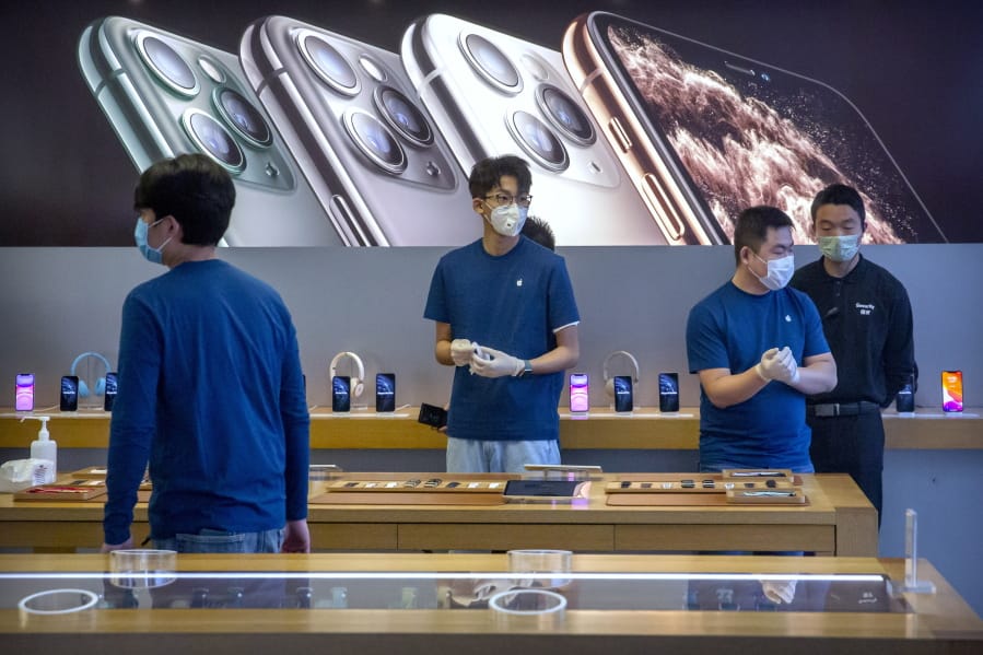 FILE - In a Feb. 14, 2020 file photo, employees wear face masks as they stand in a reopened Apple Store in Beijing. Apple Inc. is warning investors that it won&#039;t meet its second-quarter financial guidance because the viral outbreak in China has cut production of iPhones. The Cupertino, California-based company said Monday, Feb. 17, 2020 that all of its iPhone manufacturing facilities are outside Hubei province, and all have been reopened, but production is ramping up slowly.