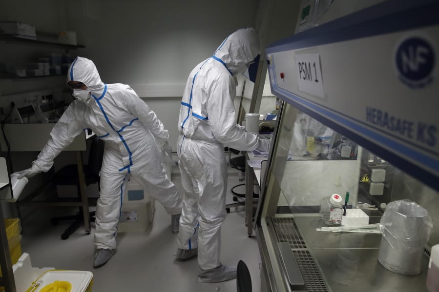 French lab scientists in hazmat gear inserting liquid in test tube manipulate potentially infected patient samples at Pasteur Institute in Paris, Thursday, Feb. 6, 2020. Scientists at the Pasteur Institute developed and shared a quick test for the new virus that is spreading worldwide, and are using genetic information about the coronavirus to develop a potential vaccine and treatments.