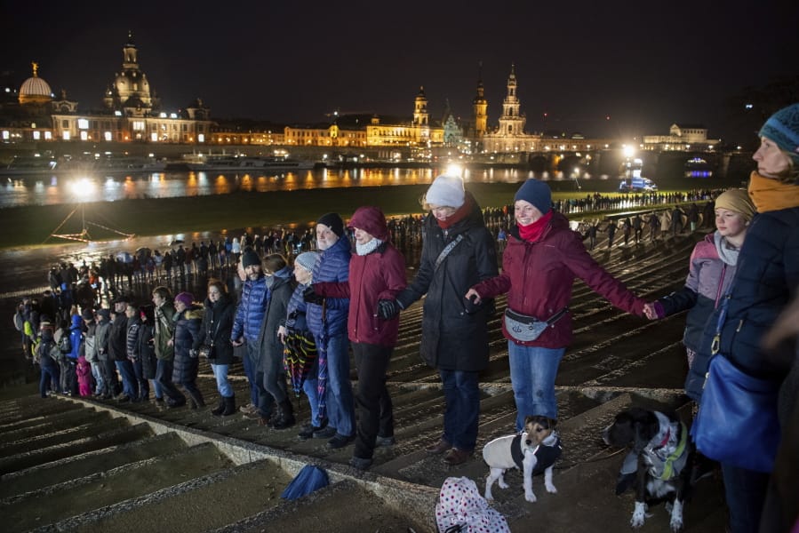 People form a human chain on the banks of the Elbe river with the historical old town in background, marking the 75th anniversary of the destruction of Dresden in the Second World War, in Dresden, Germany, Thursday Feb. 13, 2020.