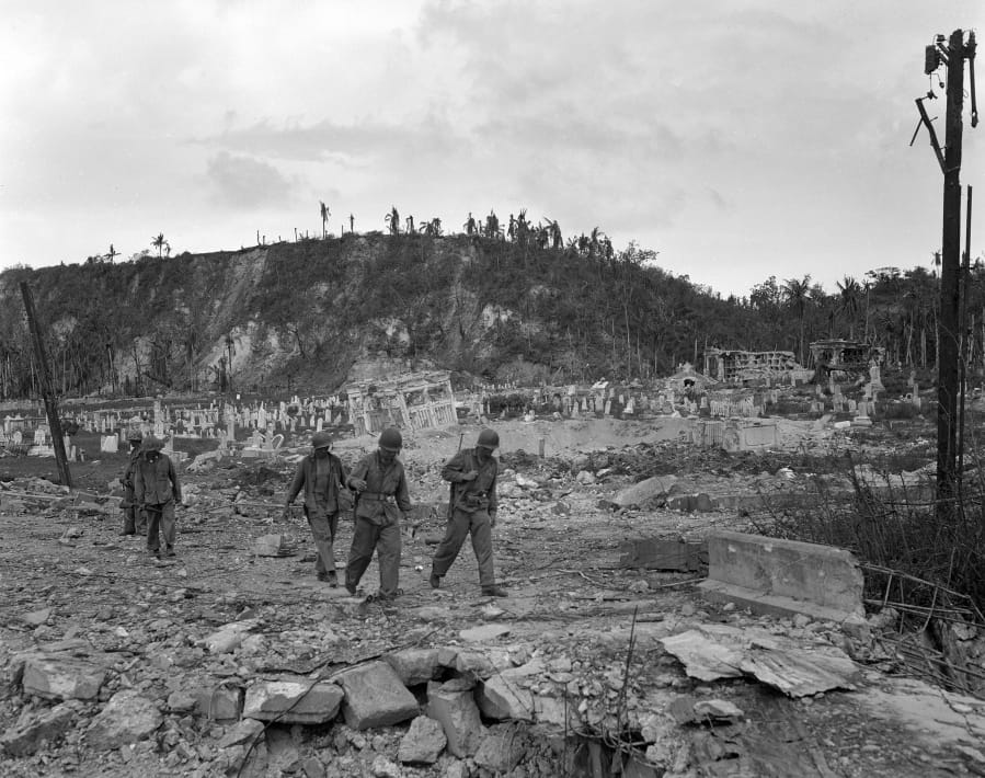FILE - In this Aug. 9, 1944 file photo, U.S. soldiers walk by a bombed out cemetery in Agana, Guam. The 1941 Japanese invasion of Guam, which happened on the same December day as the attack on Hawaii&#039;s Pearl Harbor, set off years of forced labor, internment, torture, rape and beheadings.  Now, more than 75 years later, thousands of people on Guam, a U.S. territory, are expecting to get long-awaited compensation for their suffering at the hands of imperial Japan during World War II.