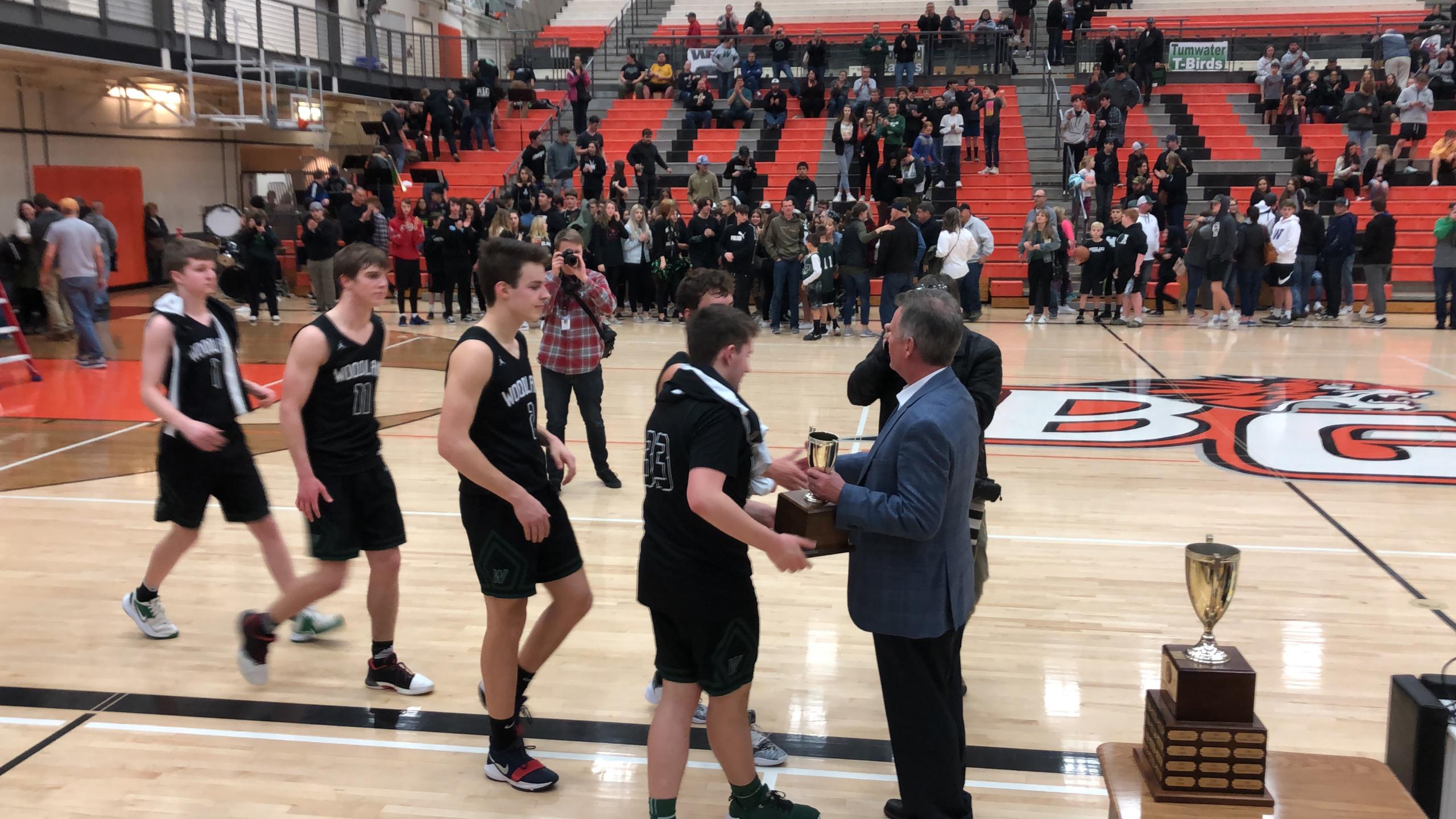 The Woodland boys basketball team receives the 2A district tournament runner-up trophy from tournament director Rob Blackman after a 63-28 loss to Tumwater in the championship game Friday at Battle Ground High School.