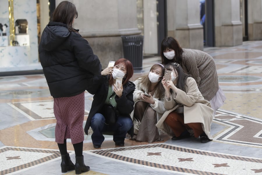 Tourists, wearing face masks, pose for a selfie in downtown Milan, Italy, Thursday, Feb. 27, 2020. In Europe, an expanding cluster in northern Italy is eyed as a source for transmissions of the COVID-19 disease.