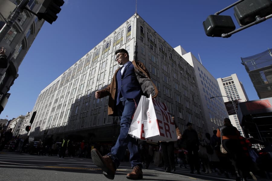 FILE - In this Nov. 29, 2019, file photo, man carries shopping bags across the street from a Macy&#039;s store in San Francisco. Macy&#039;s says it is closing 125 of its least productive stores and cutting 2,000 corporate jobs as the struggling department store tries to reinvent itself in the age of online shopping. The moves announced Tuesday, Feb. 4, 2020, come ahead of Macy&#039;s annual investor meeting where CEO Jeff Gennette is expected to unveil a three-year reinvention plan.