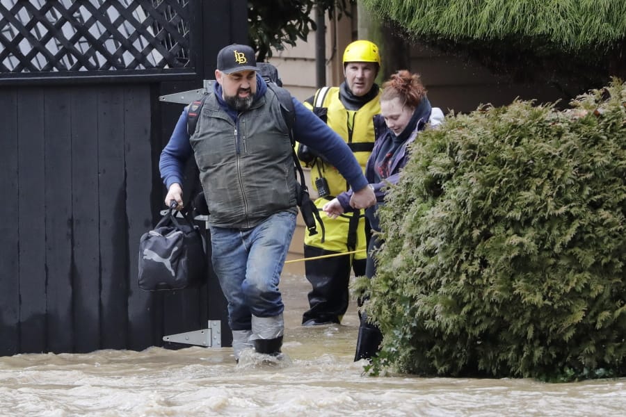 A firefighter looks on as a man escorts a woman from an apartment complex as flood waters rise Thursday, Feb. 6, 2020, in Issaquah, Wash. Heavy rain sent the creek over a major roadway, under an apartment building east of Seattle and up to the foundations of homes as heavy rains pounded the region. A flood watch was in effect through Friday afternoon across most of western Washington. Numerous roads were closed because of water over the roadway. Officials also warned of landslide risks.