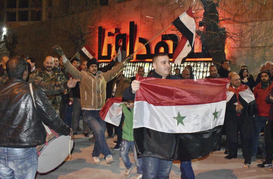 In this photo released by the Syrian official news agency SANA, Syrians celebrate as they hold their national flags in Aleppo province, Syria, Monday, Feb. 17, 2020.