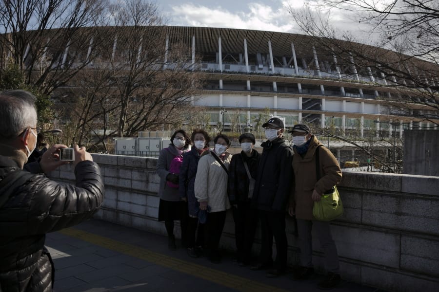 Tourists wear masks as they pause for photos with the New National Stadium, a venue for the opening and closing ceremonies at the Tokyo 2020 Olympics, Sunday, Feb. 23, 2020, in Tokyo. (AP Photo/Jae C.