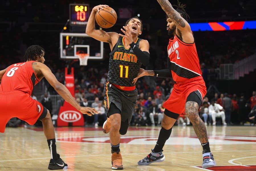 Atlanta Hawks guard Trae Young (11) tries to penetrate the defense of Portland Trail Blazers forward Trevor Ariza (8) and guard Gary Trent Jr. (2) during the first half of an NBA basketball game Saturday, Feb. 29, 2020, in Atlanta.