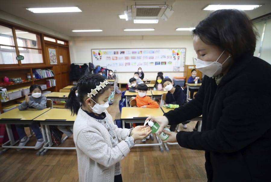 FILE - In this Jan. 30, 2020, file photo, a teacher dispenses hand sanitizer to a student at Yongsan elementary school in Seoul, South Korea. On Friday, Feb. 21,2020, South Korean Prime Minister Chung Se-kyun said the government would have to shift its focus from quarantine and border control to slowing the spread of the virus, as schools and churches were closed and some mass gatherings banned.