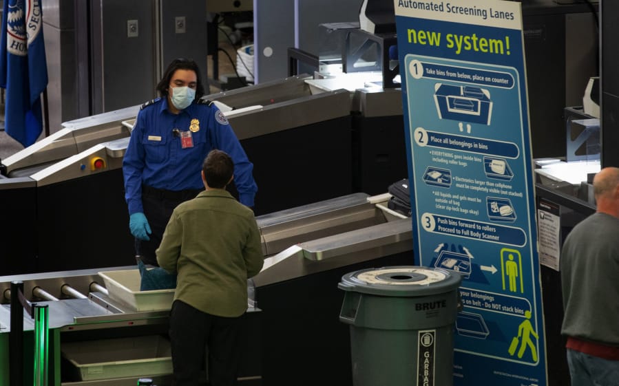 A TSA worker wears a mask while helping travelers get through Security Checkpoint 1 at Seattle-Tacoma International Airport Tuesday, March 3, 2020. (Ellen M.