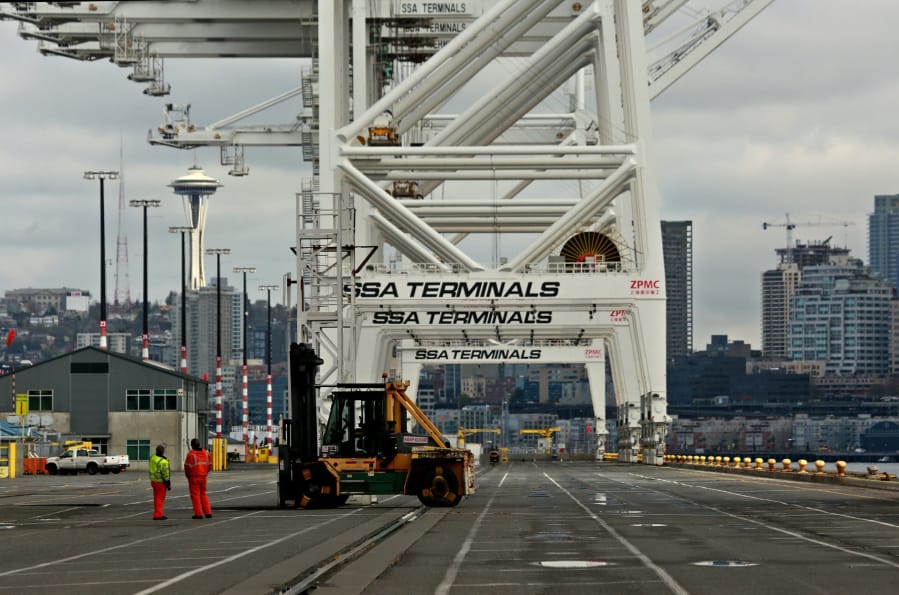 Longshoremen work below container gantry cranes at the Port of Seattle&#039;s container yard at Terminal 18, the Space Needle can be seen, behind.