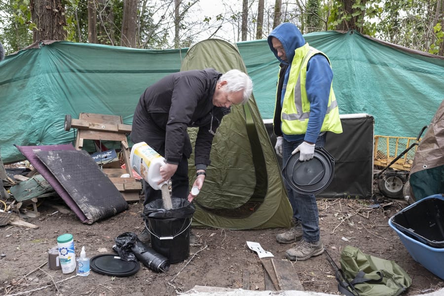 Mark Lloyd, left, shows Eric Smith how to hygenically manage a toilet he and others in his homeless camp can use on Tuesday. Smith is a homeless man who is doing what he can to keep his encampment clean. He&#039;s getting help from Lloyd who has provided some basic elements of sanitation few homeless sites have.