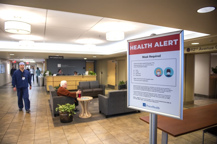 A medical worker walks past a sign informing visitors of health safety measures meant to prevent the spread of coronavirus at an entrance to PeaceHealth Southwest Medical on Monday afternoon.