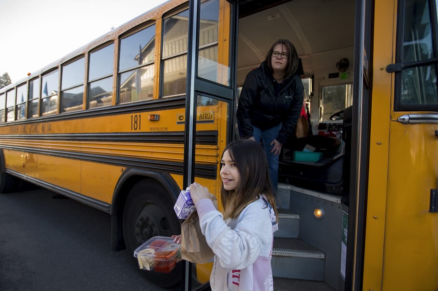 Kamryn Tanioka, 9, foreground, picks up her breakfast and lunch from school bus driver Tanisha Cardiel as she makes deliveries for students on her route in east Vancouver on Tuesday morning. Evergreen Public Schools is delivering meals to students by bus, and started the service on Tuesday.