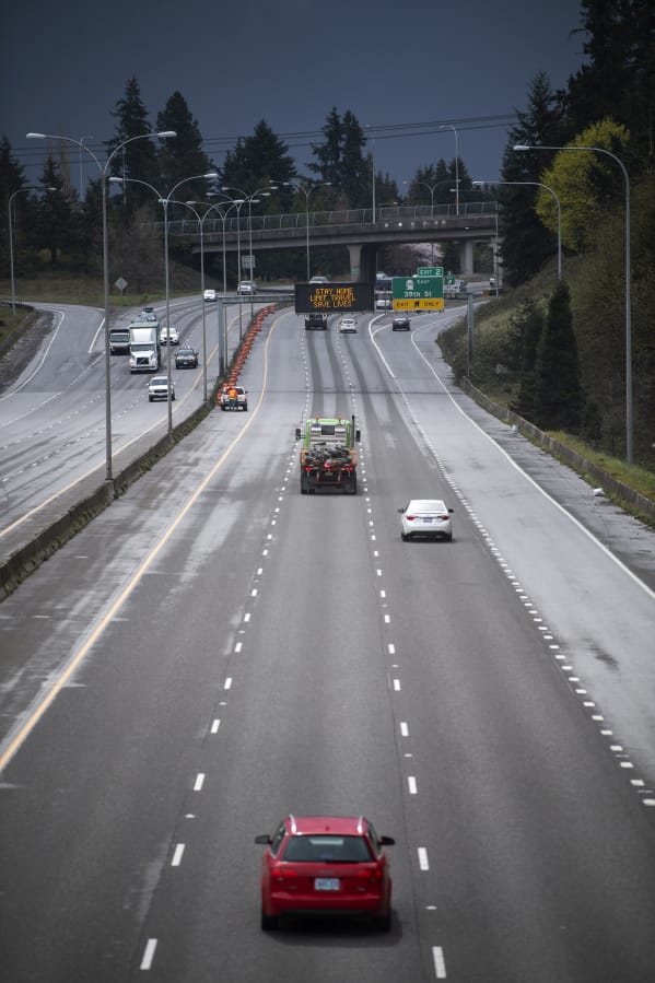 A sparse but steady flow of vehicles moves under a sign on Interstate 5 reading &quot;STAY HOME, LIMIT TRAVEL, SAVE LIVES&quot; in Vancouver on Tuesday. Gov. Jay Inslee issued a temporary stay-at-home order Monday evening to slow the spread of COVID-19.