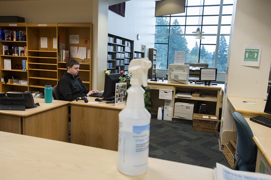 A bottle of disinfectant is seen on the front desk of the library at Washington State University Vancouver as junior Travis Lynn works nearby amid concerns of COVID-19 on Wednesday morning. Campus closed Wednesday afternoon following Gov. Jay Inslee&#039;s &quot;Stay Home, Stay Healthy&quot; order to stop the spread of COVID-19.