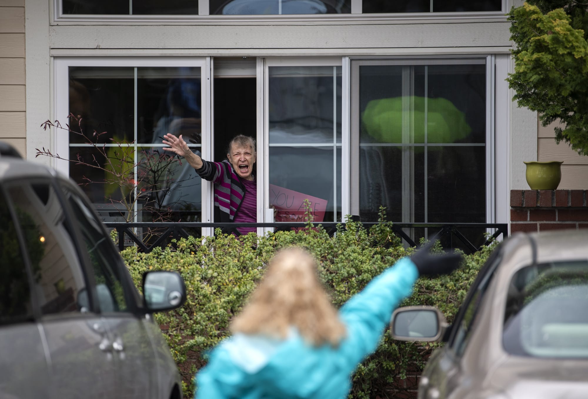 Touchmark resident Gladys Meier waves at staff members as an outdoor parade moves by her window through the parking lot at the senior living community in Vancouver on Thursday.