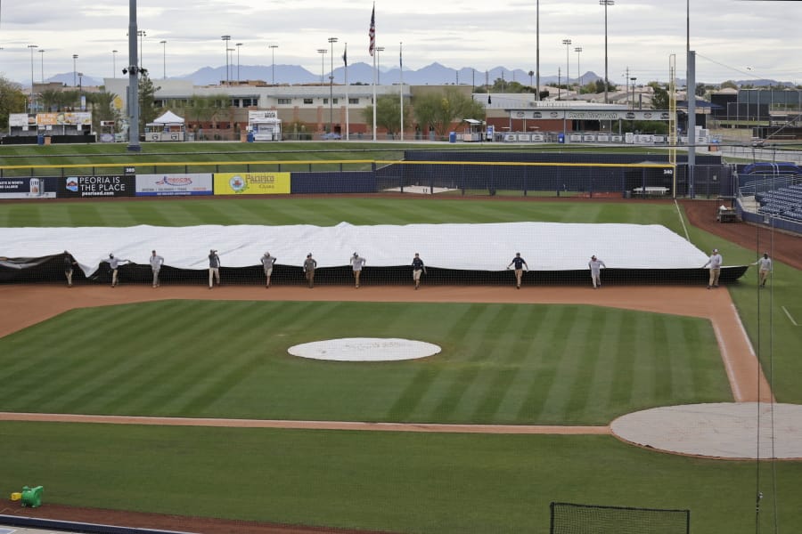 Grounds crew members pull a tarp toward the infield to cover it in anticipation of coming rain after a spring training baseball game between the Los Angeles Angels and the Seattle Mariners Tuesday, March 10, 2020, in Peoria, Ariz.