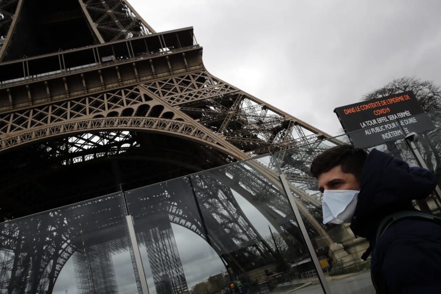 A man wearing a mask walks pasts the Eiffel tower closed after the French government banned all gatherings of over 100 people to limit the spread of the virus COVID-19, in Paris, Saturday, March 14, 2020. For most people, the new coronavirus causes only mild or moderate symptoms. For some it can cause more severe illness, especially in older adults and people with existing health problems.