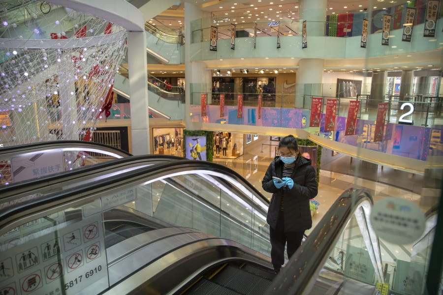 FILE - In this Friday, Feb. 28, 2020 file photo, a woman wearing a face mask and gloves rides an escalator at a mostly empty shopping mall in Beijing. The growing fear over a new virus has transformed busy streets and shopping centers into ghost towns in parts of China, Japan and Italy. Now, with the COVID-19 disease spreading in the U.S., it could deal a major blow to the country&#039;s over 1,000 malls at time when many of them are already struggling with a slew of retail bankruptcies.