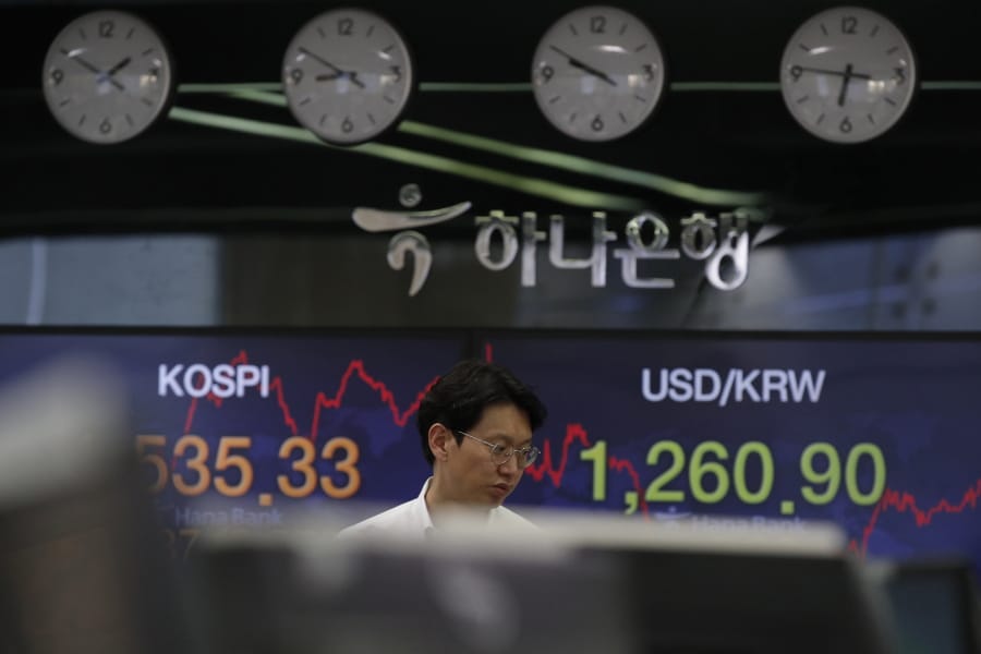 A currency trader walks by screens showing the Korea Composite Stock Price Index (KOSPI), left, and the foreign exchange rate between U.S. dollar and South Korean won at the foreign exchange dealing room in Seoul, South Korea, Tuesday, March 24, 2020. Asian stock markets gained Tuesday after the U.S. Federal Reserve promised support to the struggling economy as Congress delayed action on a $2 trillion coronavirus aid package.