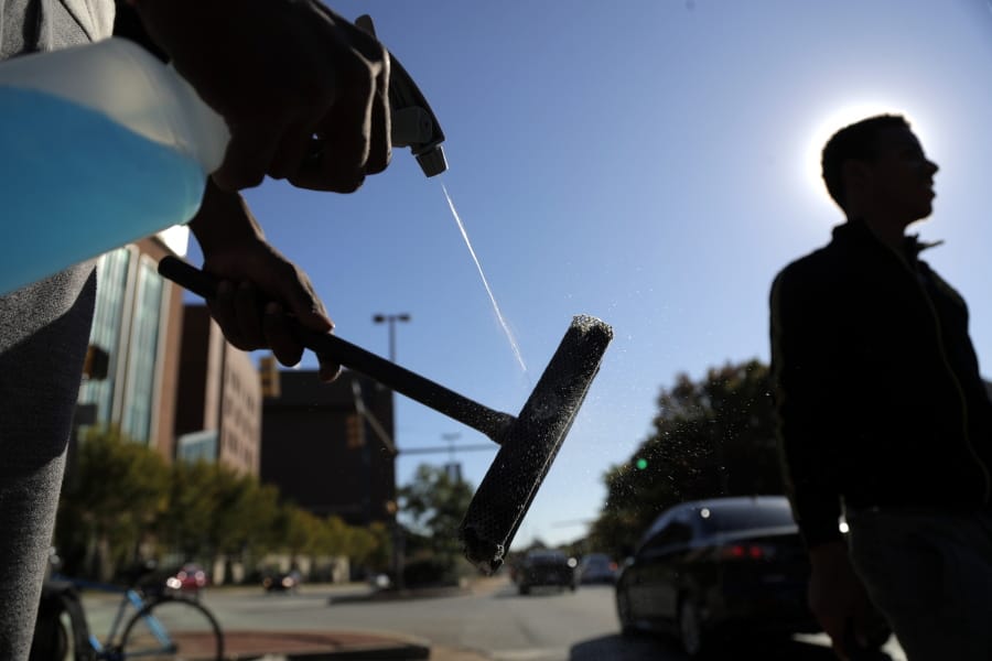 In a photo taken Thursday, Oct. 24, 2019, Jerome Holloway, left, sprays his squeegee as he and another teenager walks by as they work a corner in Baltimore.  A debate over Baltimore&#039;s so-called squeegee kids is reaching a crescendo as the city grapples with issues of crime and poverty and a complicated history with race relations. Officials estimate 100 squeegee kids regularly work at intersections citywide, dashing into the street as red lights hit to clean windshields in exchange for cash from drivers.