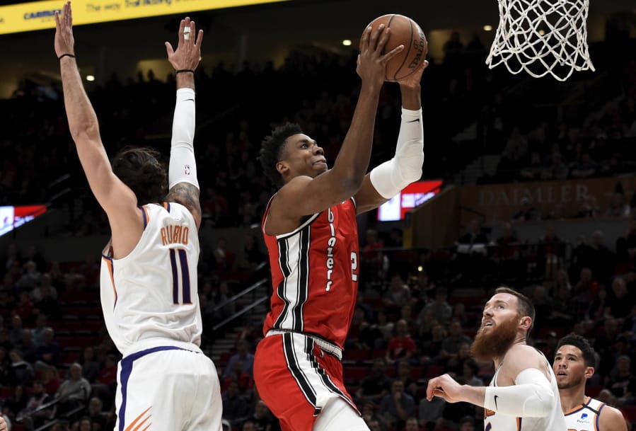 Portland Trail Blazers center Hassan Whiteside, center, drives to the basket on Phoenix Suns guard Ricky Rubio, left, and center Aron Baynes, right, during the first quarter of an NBA basketball game in Portland, Ore., Tuesday, March 10, 2020.