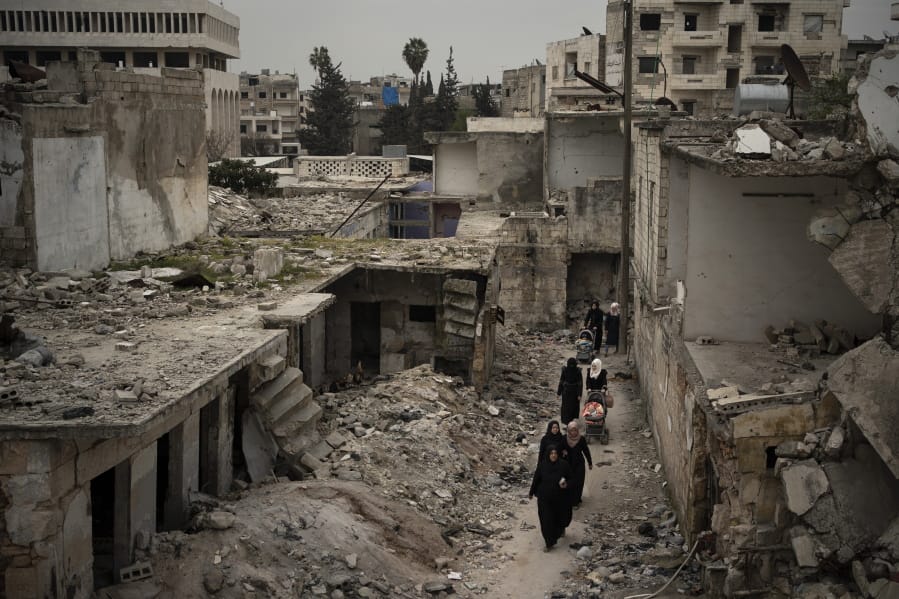In this Thursday, March 12, 2020 photo, women walk in a neighborhood heavily damaged by airstrikes in Idlib, Syria. Idlib city is the last urban area still under opposition control in Syria, located in a shrinking rebel enclave in the northwestern province of the same name. Syria&#039;s civil war, which entered its 10th year Monday, March 15, 2020, has shrunk in geographical scope -- focusing on this corner of the country -- but the misery wreaked by the conflict has not diminished.