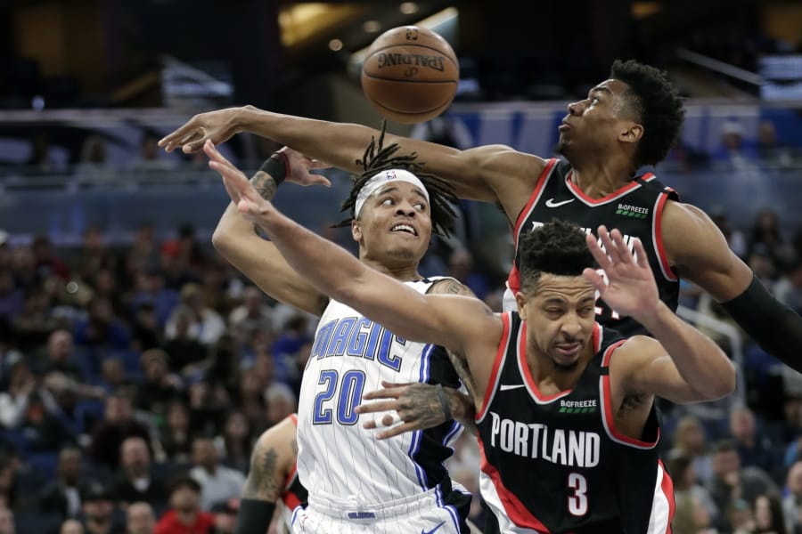 Orlando Magic guard Markelle Fultz (20) passes the ball behind his head as he gets trapped between Portland Trail Blazers center Hassan Whiteside, back right, and guard CJ McCollum (3) during the second half of an NBA basketball game, Monday, March 2, 2020, in Orlando, Fla.