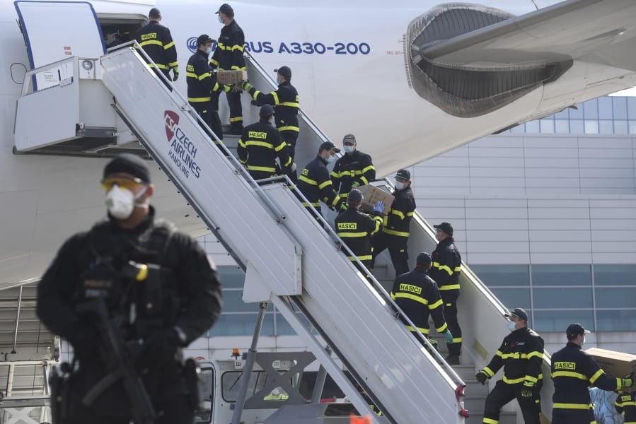 A police officer stands guard as firefighters unload an airplane Friday at the Vaclav Havel Airport in Prague. The plane brought medical aid and protective equipment from China.