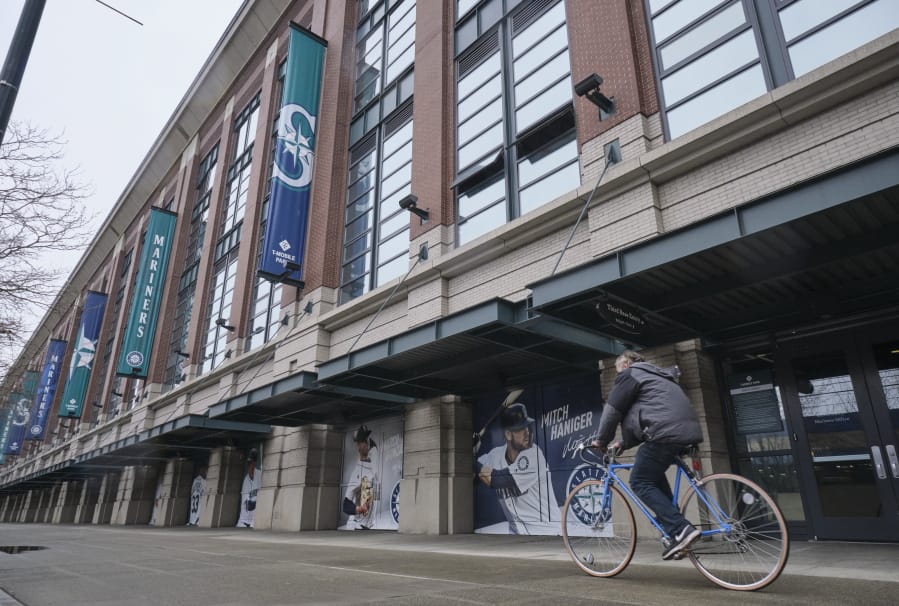 A bicyclist rides past T-Mobile Park, Wednesday, March 11, 2020, in Seattle, where baseball&#039;s Seattle Mariners plays home games. In efforts to slow the spread of the COVID-19 coronavirus, Washington State Gov. Jay Inslee announced a ban on large public gatherings in three counties in the metro Seattle area. That decision impacts the Seattle Mariners, Seattle Sounders, and the XFL&#039;s Seattle Dragons home games.