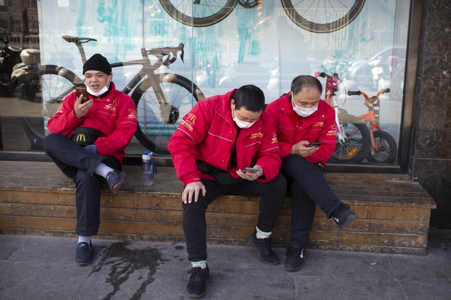 McDonald&#039;s deliverymen wear face masks as they wait for orders outside a restaurant in Beijing, Saturday, March 7, 2020. Crossing more borders, the new coronavirus hit a milestone, infecting more than 100,000 people worldwide as it wove itself deeper into the daily lives of millions, infecting the powerful, the unprotected poor and vast masses in between.