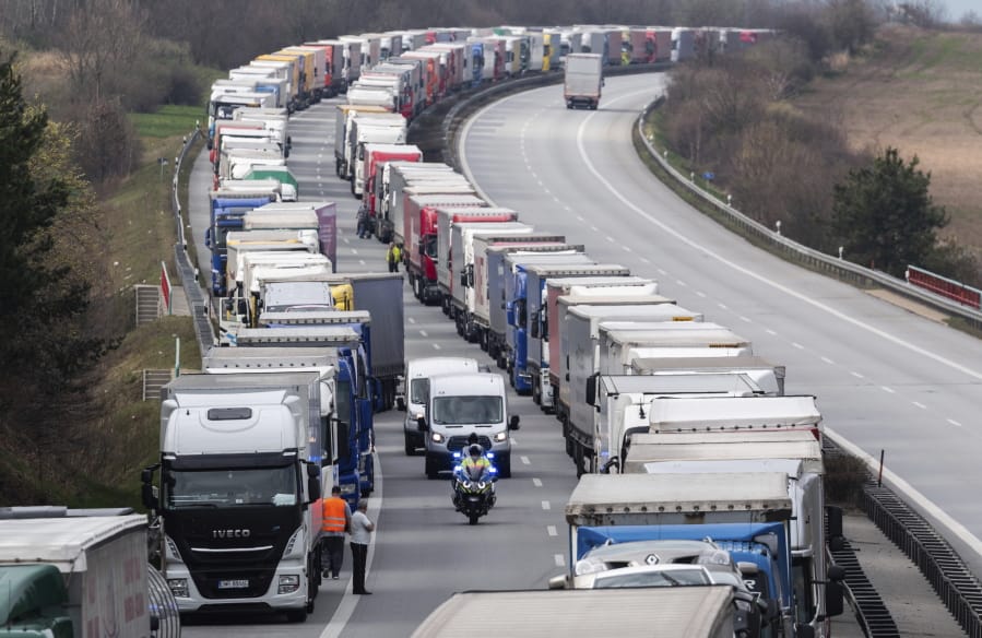 A German police officer drive on a  motorcycles between trucks, which jam on the motorway A4 near Goerlitz, Germany, Thursday, March 19, 2020. Thousands of truck drivers have to hold out in a traffic jam, which has grown to a length of about 40 kilometers, before the border with Poland.
