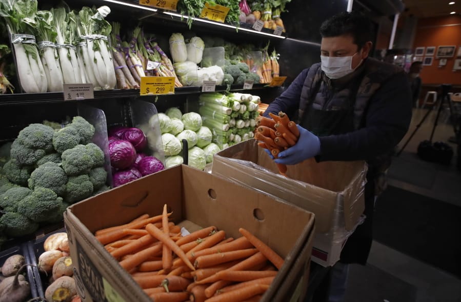 A worker, wearing a protective mask against the coronavirus, stocks produce before the opening of Gus&#039;s Community Market, on Friday in San Francisco.