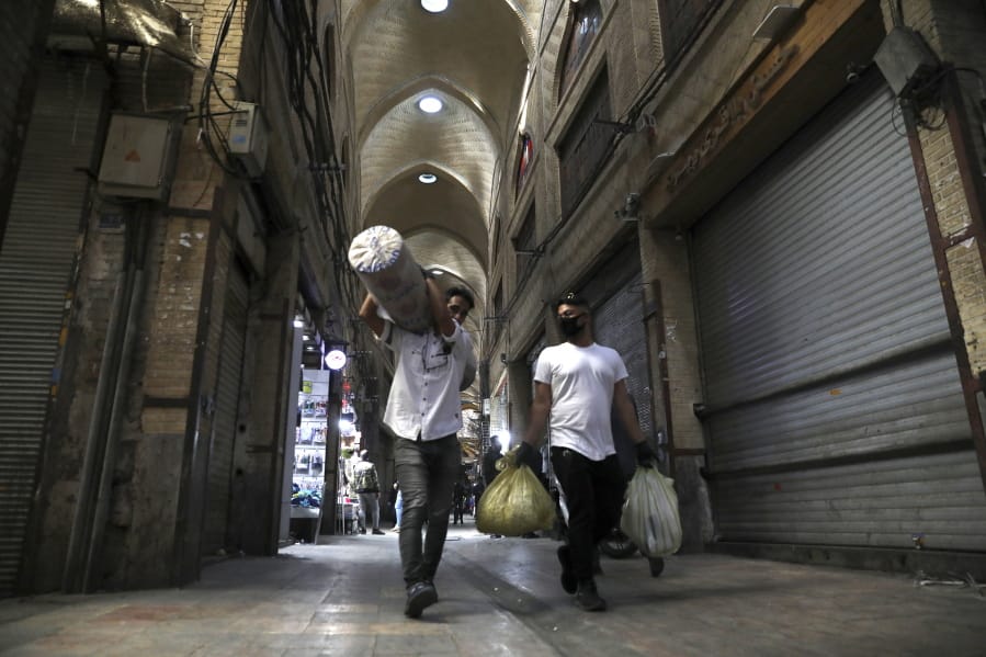In this Tuesday, March 17, 2020, photo, men carry their goods through mostly closed Tehran&#039;s Grand Bazaar, Iran. The new coronavirus ravaging Iran is cutting into celebrations marking the Persian New Year, known as Nowruz.