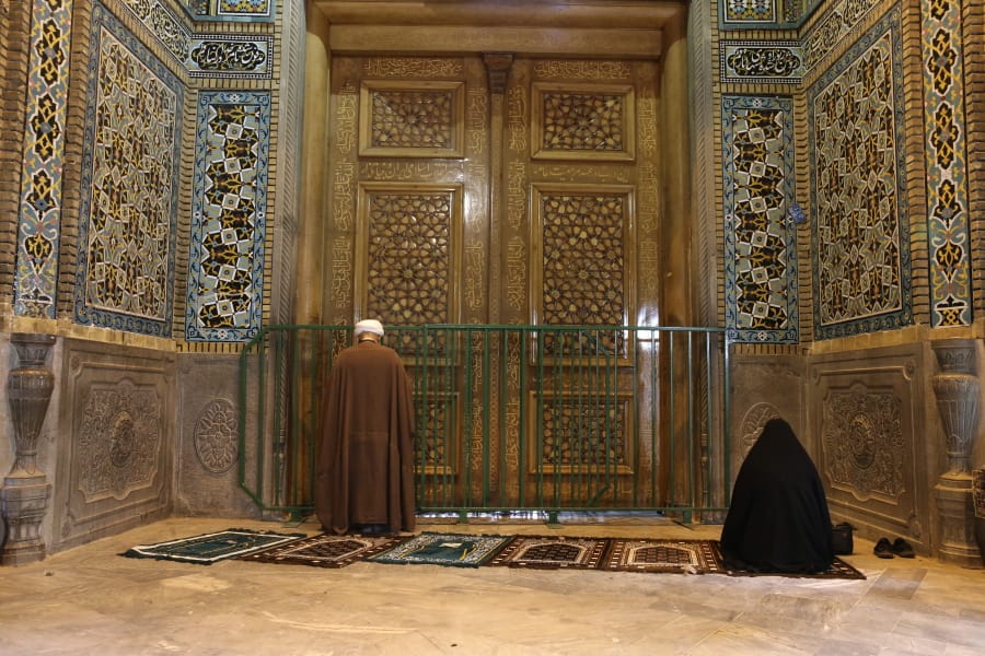 A cleric and a woman pray behind a closed door of Masoume shrine in the city of Qom, some 80 miles (125 kilometers) south of the capital Tehran, Iran, Monday, March 16, 2020. On Monday, Iran closed the Masoume shrine, a major pilgrimage site in the city of Qom, the epicenter of the country&#039;s new coronavirus outbreak. Authorities were already restricting access and barring pilgrims from kissing or touching the shrine, but it had remained open.
