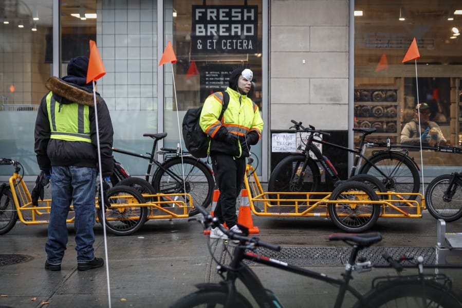 Delivery workers wearing protective gloves and face masks due to coronavirus concerns prepare to work outside a Whole Foods Market on Houston Street, Monday, March 23, 2020, in New York. An order requiring most New Yorkers stay home went into effect Sunday, part of the state&#039;s efforts to stem the coronavirus pandemic.