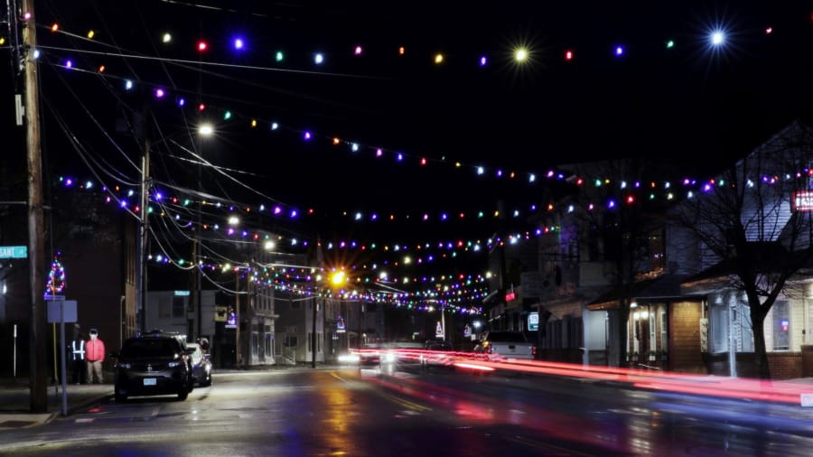 In this March 19, 2020, photo, car tail lights streak under Christmas lights recently turned back on in Farmington, N.H. As the coronavirus spreads, holiday lights are going back up to provide a bit of emotional and actual brightness.