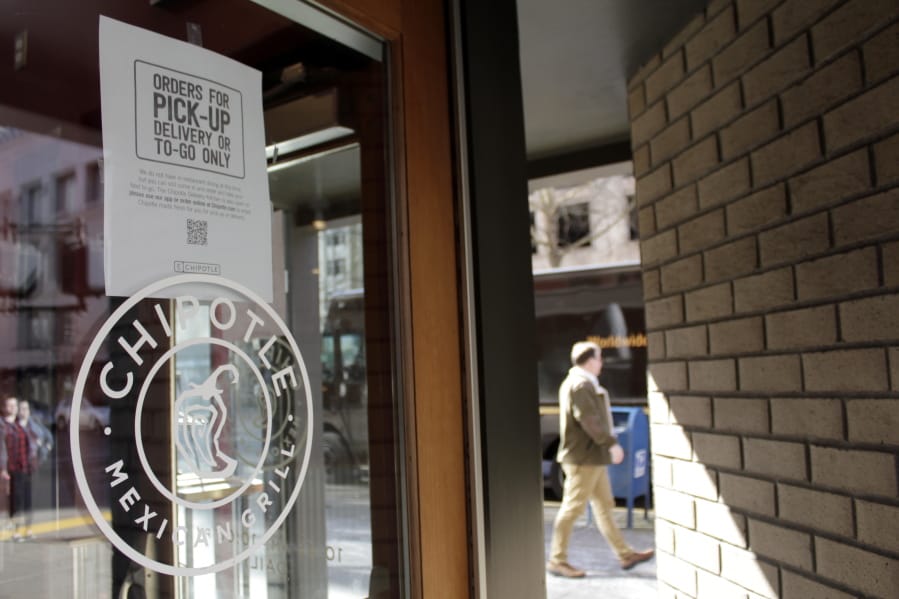 A sign indicating that only carry-out or delivery options are available hangs in the window of a closed Chipotle restaurant in Portland, Ore., Monday, March 16, 2020. Gov. Kate Brown announced a four-week ban on eat-in dining at bars and restaurants throughout the state on Monday to slow the spread of the new coronavirus in Oregon. Restaurants can still offer take-out and delivery.