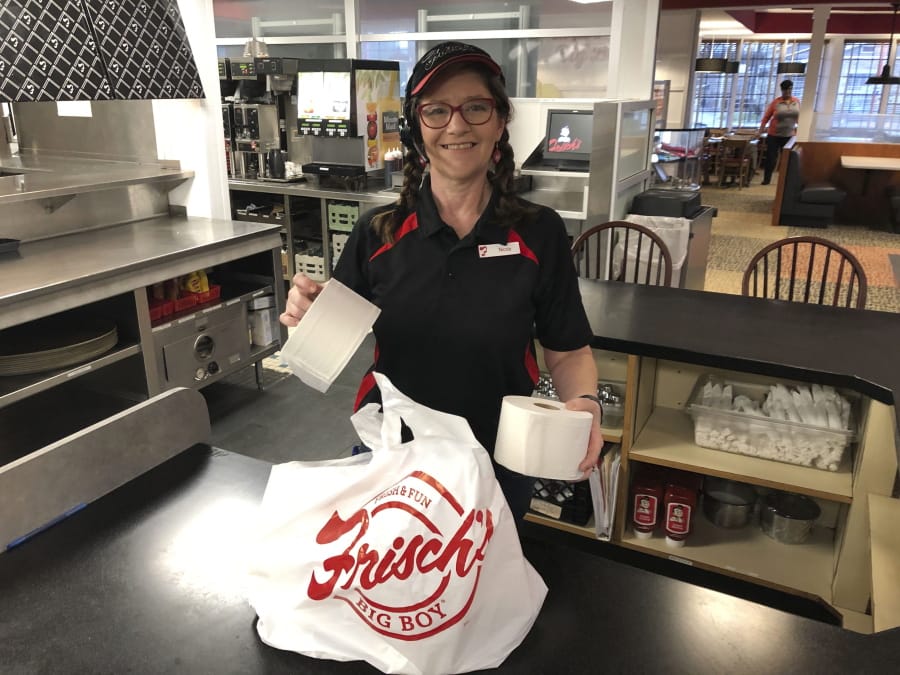 In this photo made on March 20, 2020, Frisch&#039;s Big Boy restaurant employee Nicole Cox bags up an order of toilet paper, among in-demand items including milk and bread the double-decker burger chain is now offering during the coronavirus outbreak in Cincinnati, Ohio.  With business sinking under coronavirus outbreak restrictions,the nation&#039;s restaurants are transforming operations and menus to try to stay afloat.