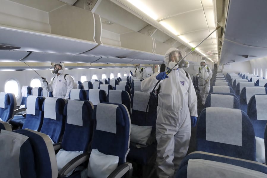 Workers wearing protective gears spray disinfectant inside a plane for New York as a precaution against the new coronavirus at Incheon International Airport in Incheon, South Korea, Wednesday, March 4, 2020. The coronavirus epidemic shifted increasingly westward toward the Middle East, Europe and the United States on Tuesday, with governments taking emergency steps to ease shortages of masks and other supplies for front-line doctors and nurses.