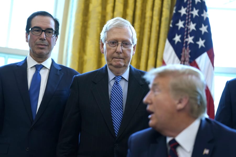 Treasury Secretary Steven Mnuchin and Senate Majority Leader Mitch McConnell, R-Ky., listen as President Donald Trump speaks before he signs the coronavirus stimulus relief package in the Oval Office at the White House, Friday, March 27, 2020, in Washington.
