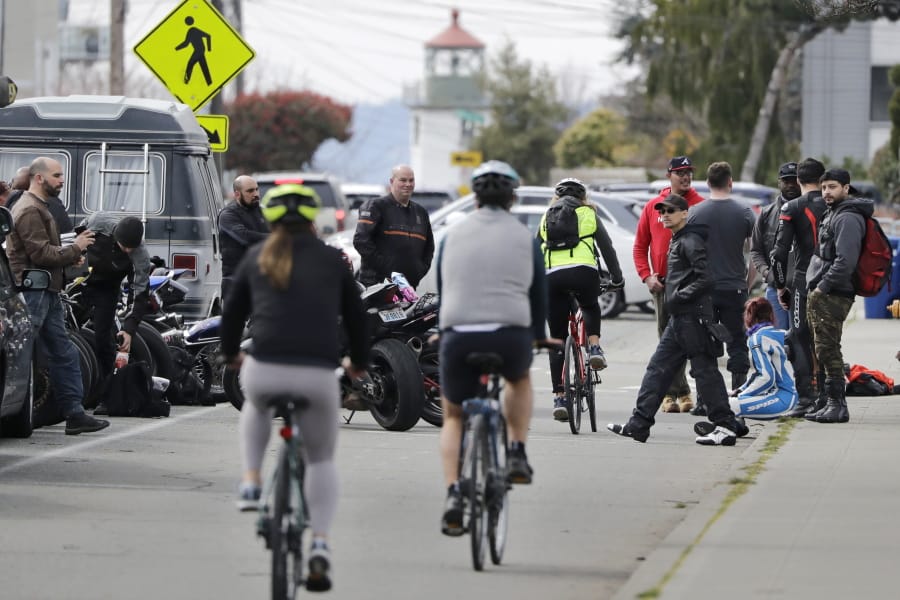 Bicyclists wind through a group gathered along a path at Alki Beach Park Sunday, March 22, 2020, in Seattle, where people are asked to maintain a physical distance of at least six feet apart in response to the coronavirus outbreak. Health officials reported Sunday that there have been at least 95 coronavirus deaths in Washington state and nearly 2,000 confirmed cases.