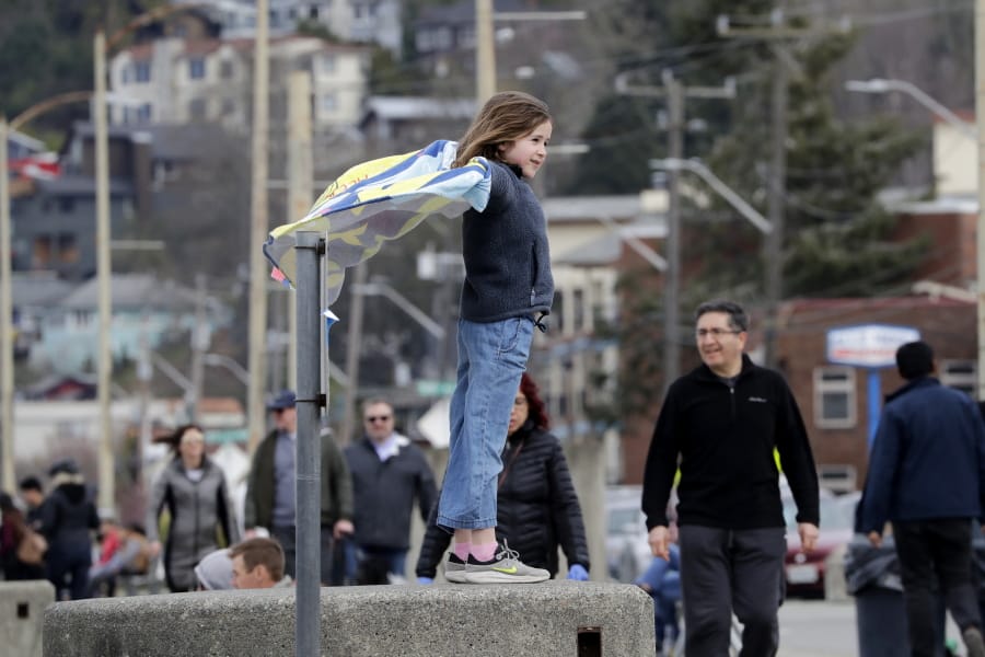 Alexandra Avery, 8, stands atop a beach wall and watches pedestrians pass by before heading out with her family from a busy city park Sunday, March 22, 2020, in Seattle. President Donald Trump on Sunday issued a disaster declaration for Washington and ordered federal assistance for the state, tribal and local response to the coronavirus outbreak that has killed dozens. Health officials reported Sunday that there have been at least 95 coronavirus deaths in Washington state and nearly 2,000 confirmed cases.