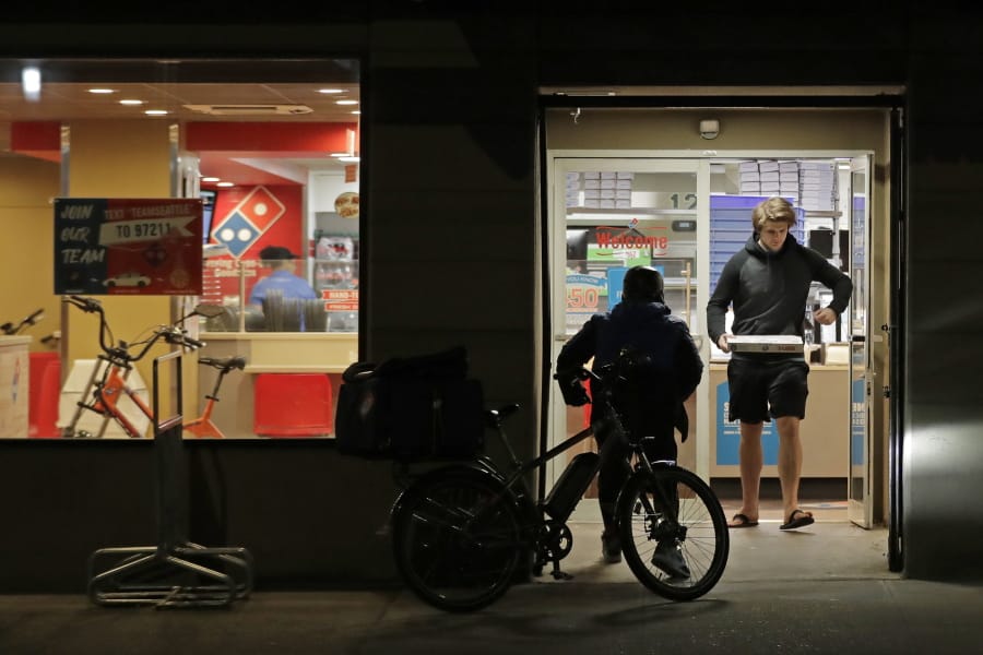 A man uses his elbow to open the door as he walks out of a Domino&#039;s Pizza restaurant in downtown Seattle as a delivery driver walks in Sunday. Washington Gov. Jay Inslee said Sunday night that he would order all bars, restaurants, entertainment and recreation facilities in the state to temporarily close to fight the spread of the COVID-19 coronavirus. Inslee said that restaurants could continue takeout and delivery services. (Ted S.