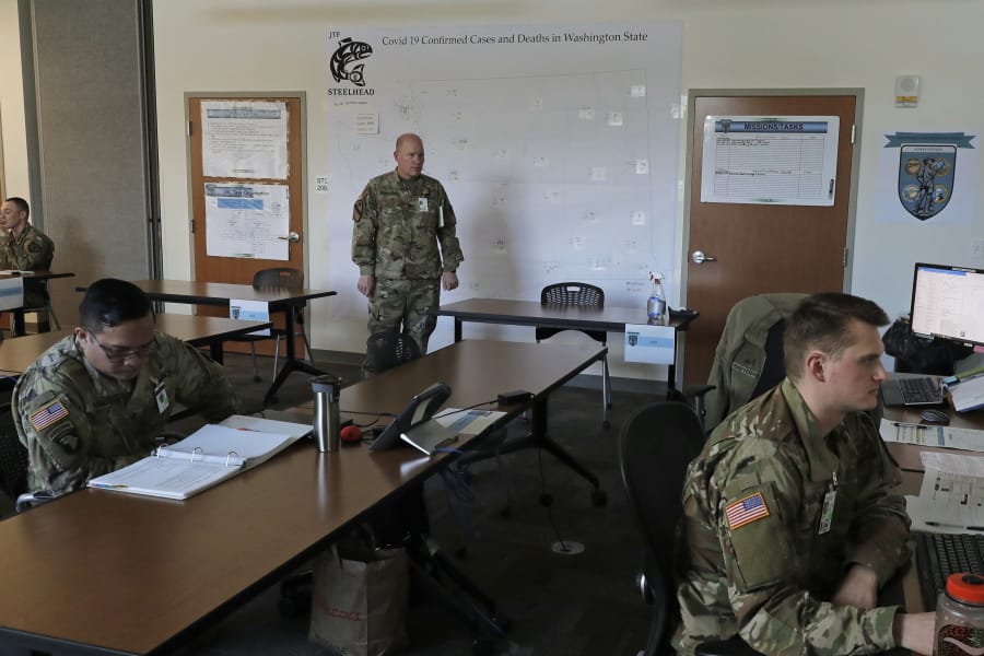 Washington Army National Guard Col. Kevin McMahan, center, on Tuesday stands next to a map of confirmed positive cases and deaths attributed to the new coronavirus in Washington as he observes activities in the operations room for the coordination of Washington National Guard troops and active-duty U.S. Army soldiers working in the state in response to the new coronavirus outbreak, at Camp Murray. (Ted S.