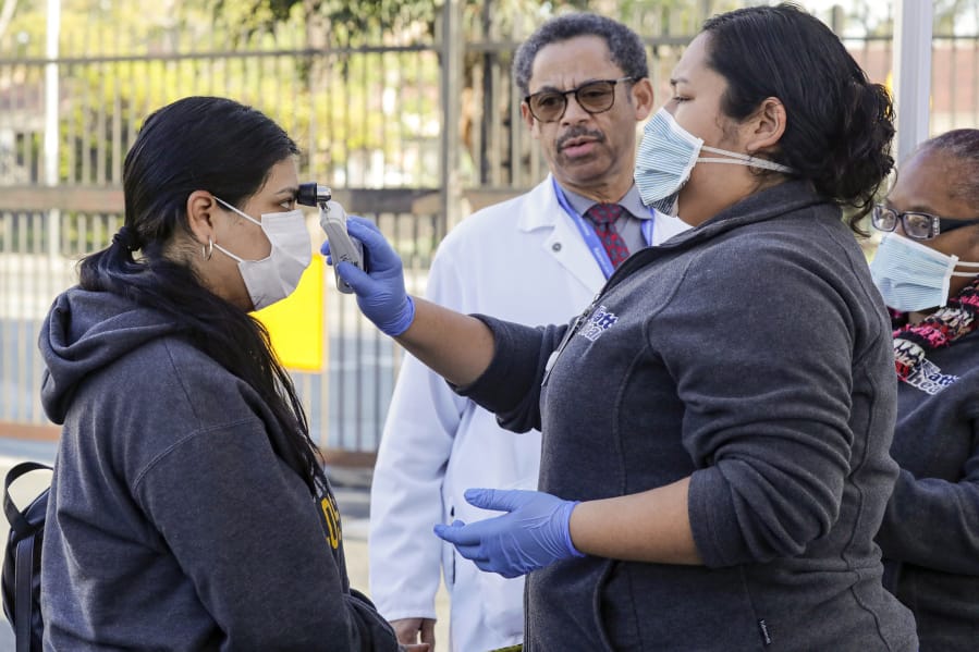 Dr. Oliver Brooks, center, looks on as health care worker Lucy Arias, right, checks a patient for fever at a COVID-19 screening station on Thursday, March 19, 2020 at Watts Health Center, Los Angeles, Calif.
