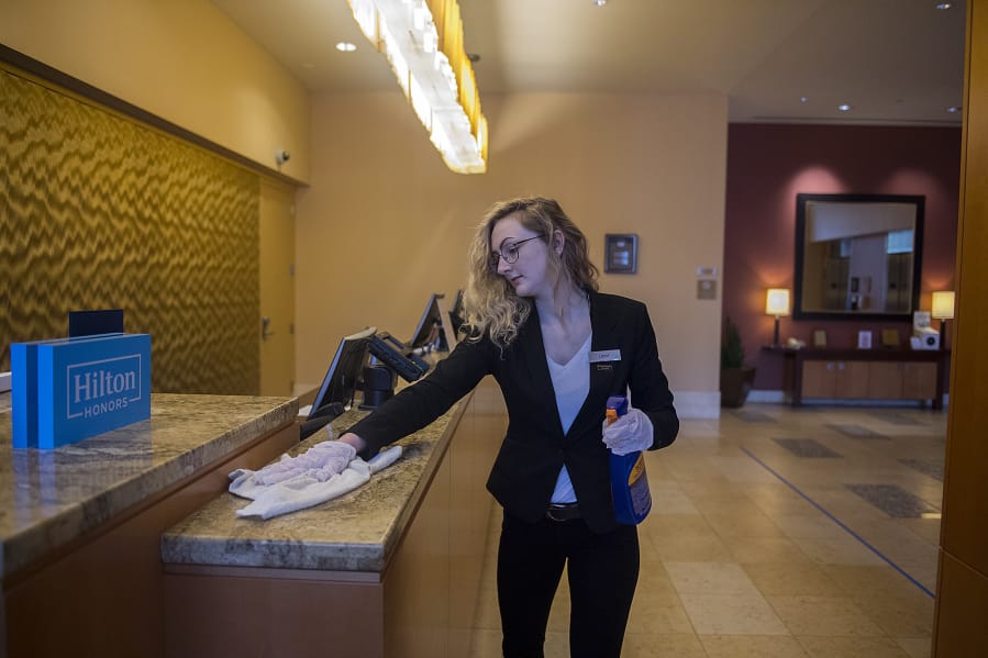 Guest service agent Libby Lusk keeps the front desk at the Hilton Vancouver Washington disinfected while working in an empty lobby on Wednesday morning. The hospitality industry has been hit hard by the COVID-19 crisis.