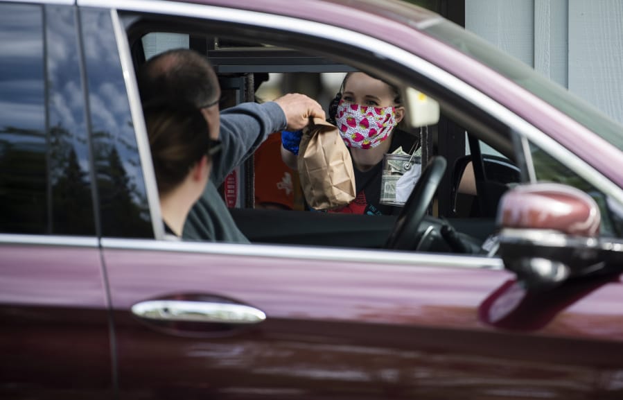 Team manager Krysta States hands an order to customers at Burgerville at the intersection of Fourth Plain Boulevard and Fort Vancouver Way. The Vancouver-based fast food chain has been operating on a drive-thru and delivery-only model since mid-March, and has instituted a number of health safety measures including issuing masks to all employees.